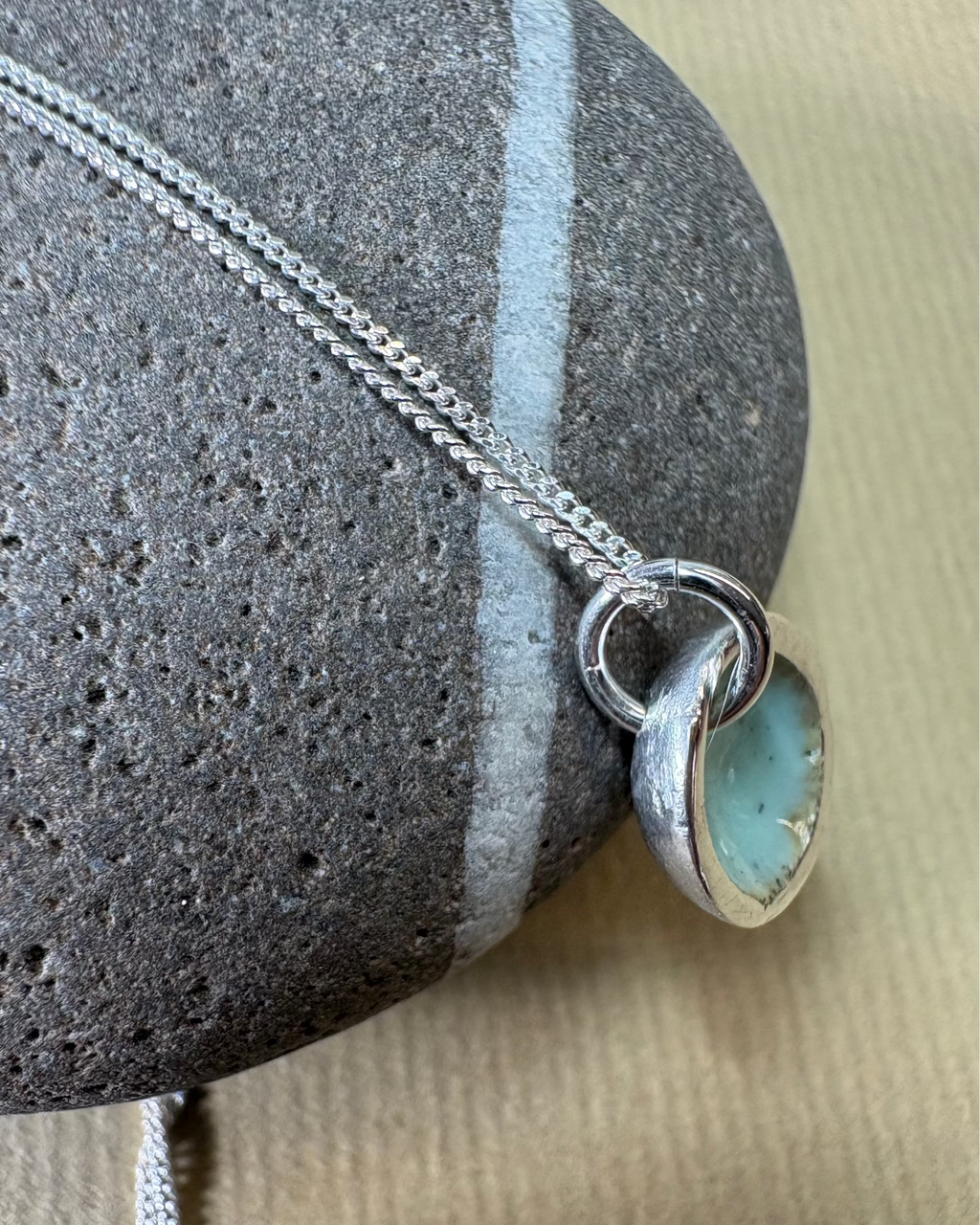 Silver pool necklace with turquoise enamel on a pebble surface