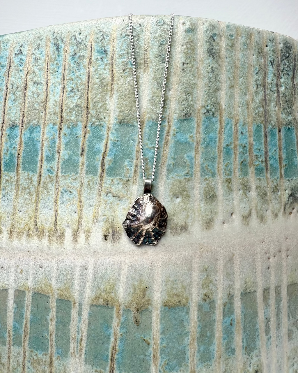 Silver limpet shell necklace with a silver chain on a  ceramic surface