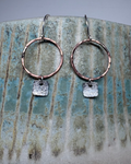 Bronze hoop earrings with textured square silver charms on a ceramic surface.