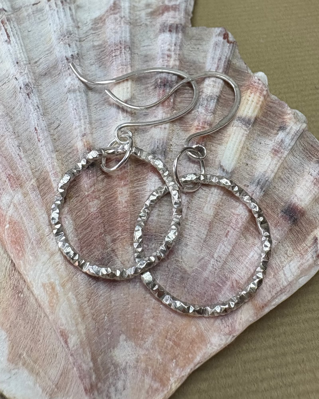 Silver wavy hoop earrings on a seashell with a beige background