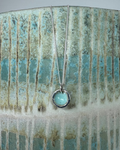 Silver pool necklace with a turquoise enamel on a textured ceramic surface