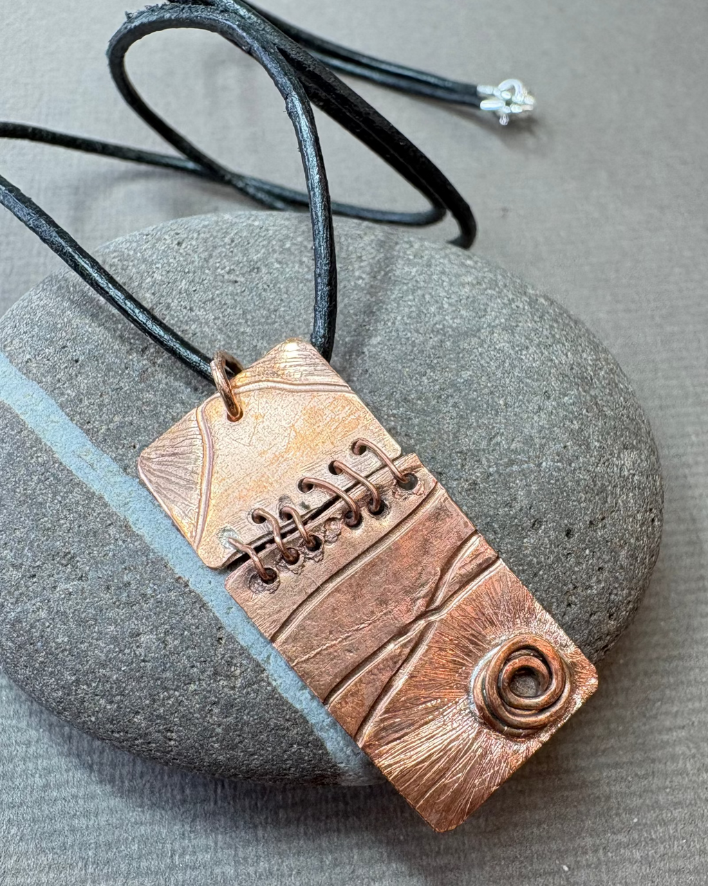 Copper art pendant necklace on a gray pebble surface