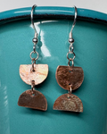 Pair of textured circular cut earrings with patina hanging from a teal cup 