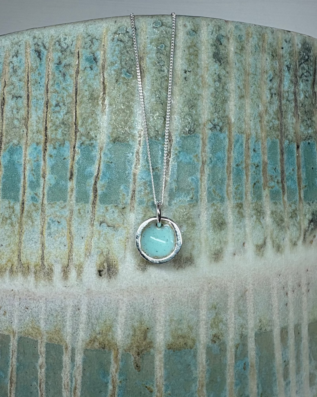 Silver pool necklace with turquoise enamel on textured ceramic surface