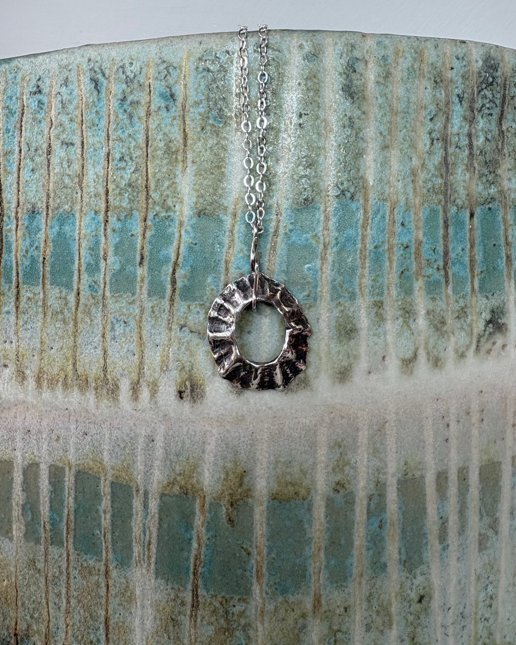 Silver sea-worn limpet shell pendant on a textured ceramic surface
