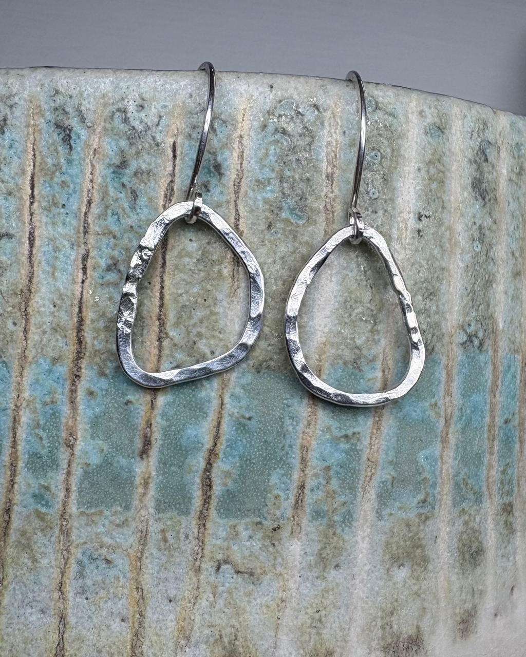Silver hammered teardrop earrings on a ceramic surface