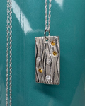 Silver rectangular necklace with wavy design featuring gold and clear stones, against a teal mug background.
