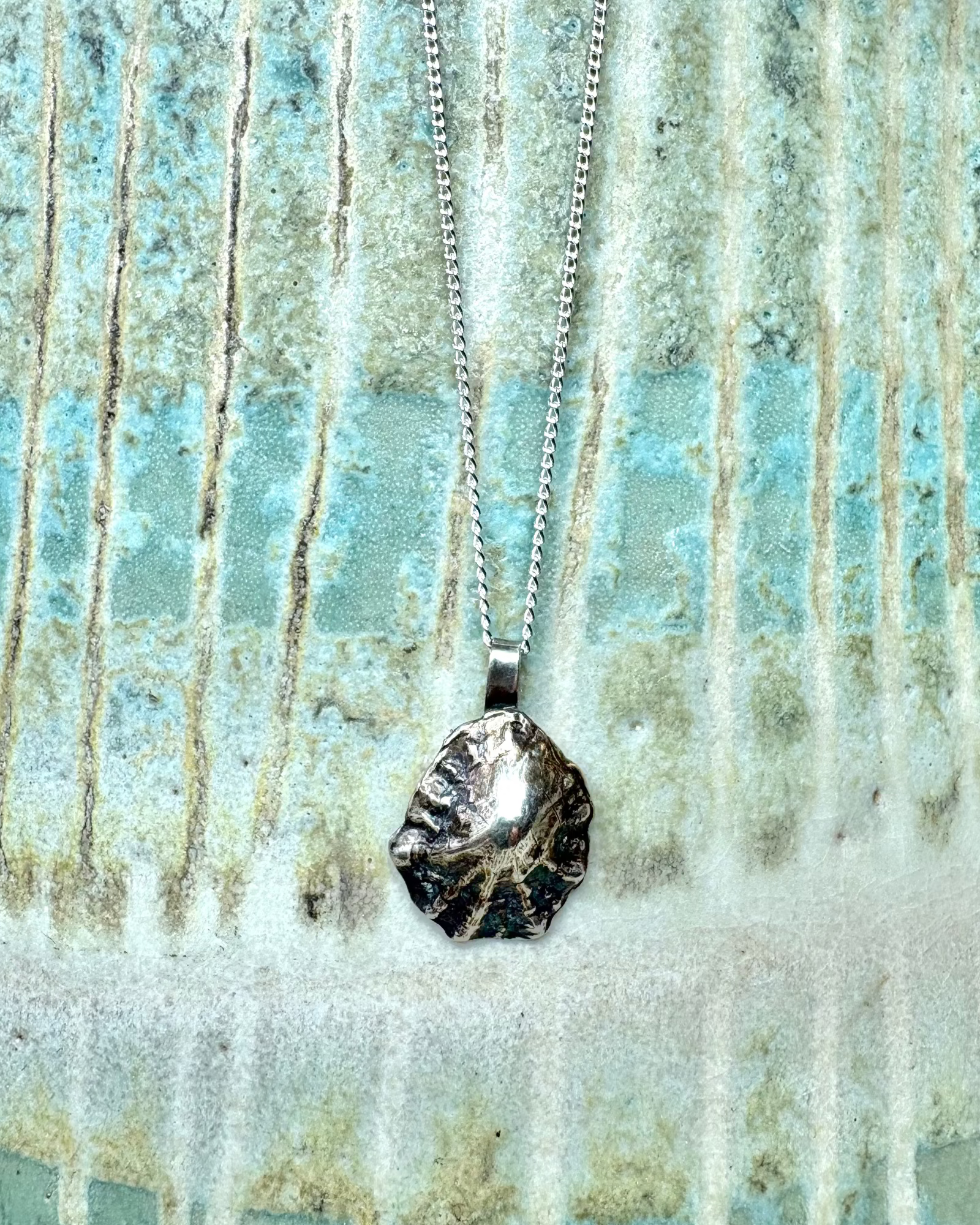Silver limpet shell necklace with silver chain hanging on a  ceramic surface