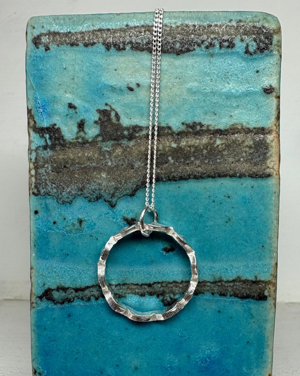 Silver wavy circular pendant necklace on a blue textured background