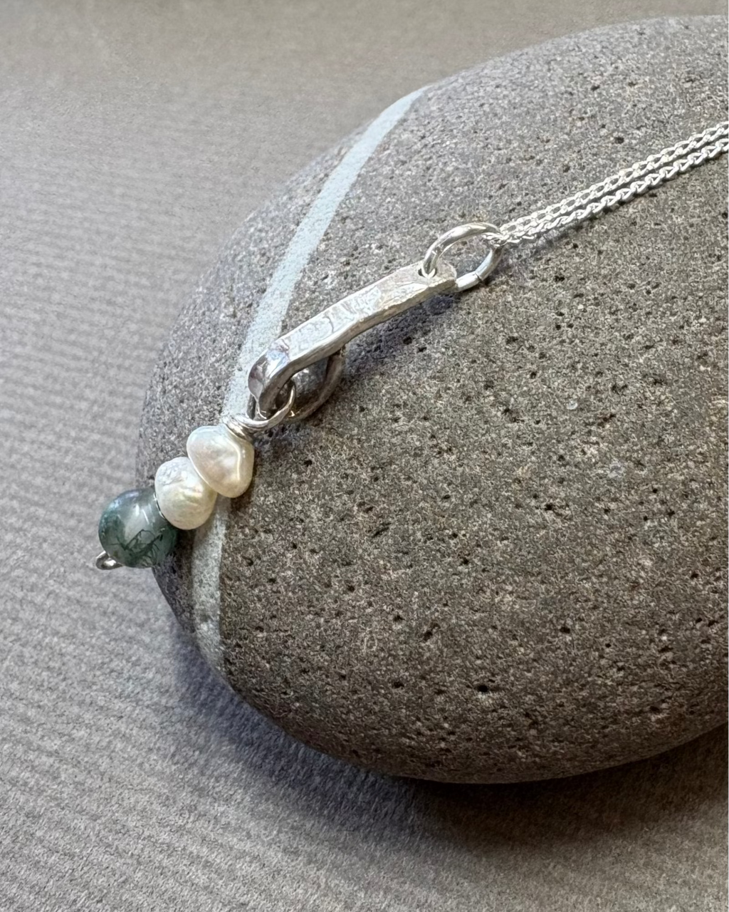 Silver necklace with pearls and moss agate beads on a pebble surface
