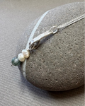 Silver necklace with pearls and moss agate beads on a pebble surface