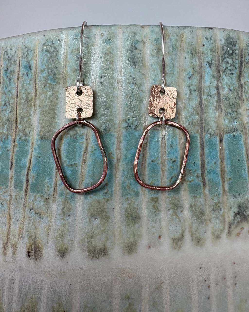 Pair of bronze hammered and textured earrings on a ceramic surface