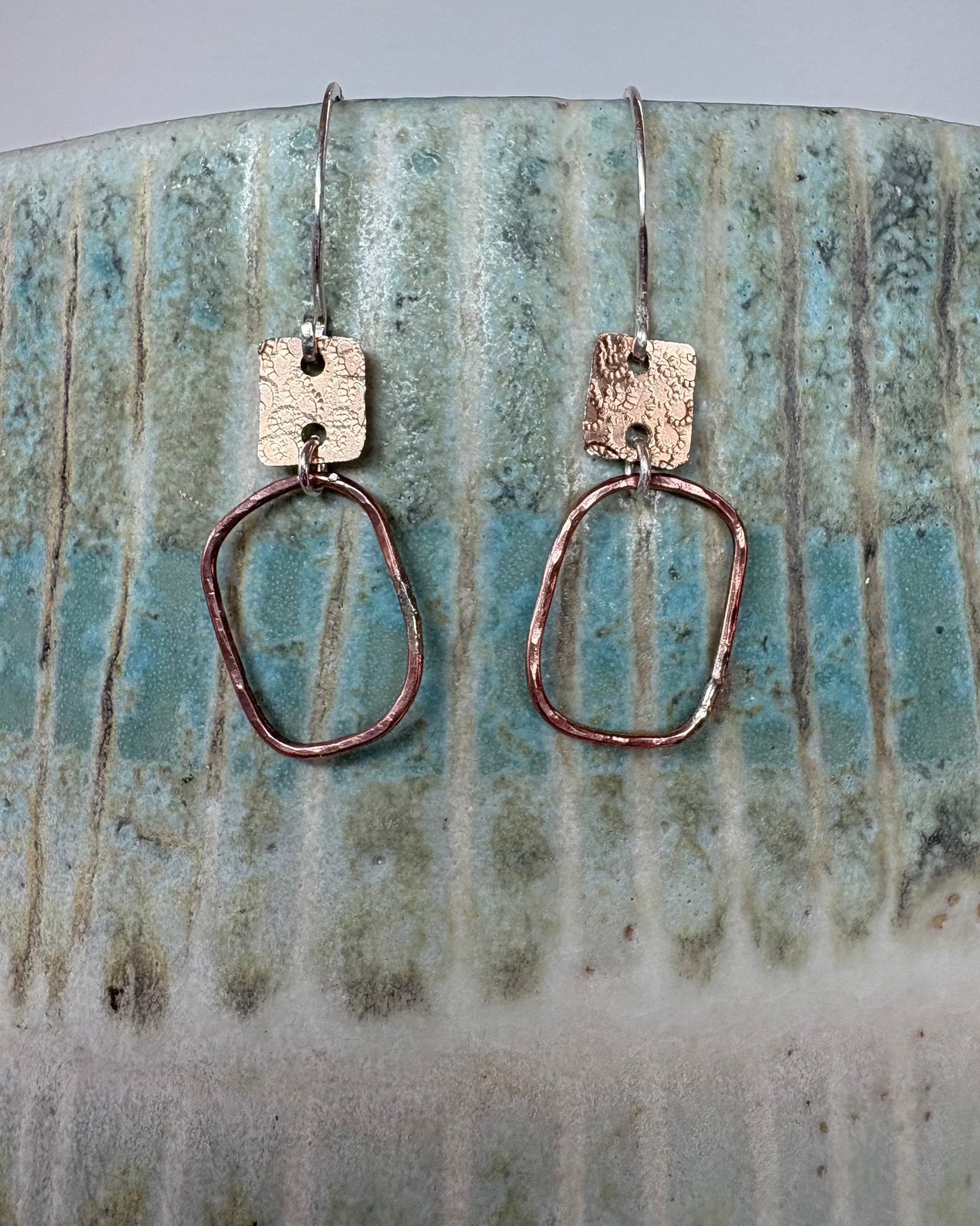 Pair of bronze hammered and textured earrings on a ceramic surface