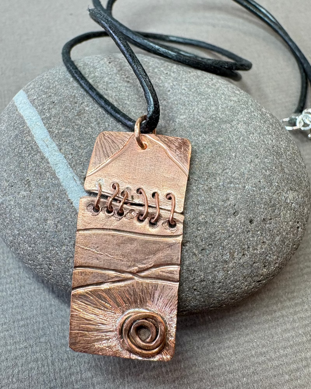 Copper sewn pendant necklace with black leather cord on a pebble
