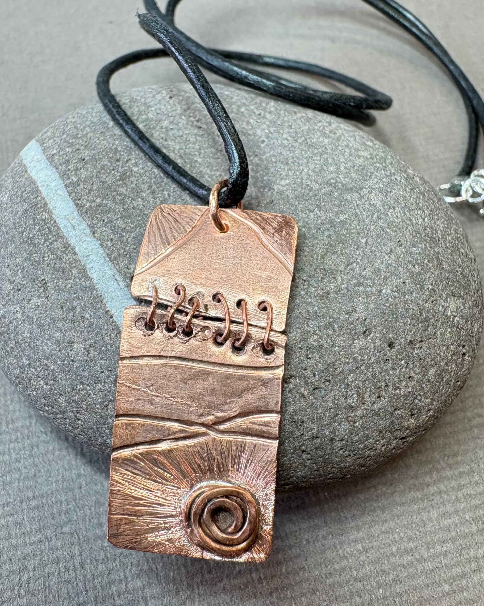 Copper sewn pendant necklace with black leather cord on a pebble