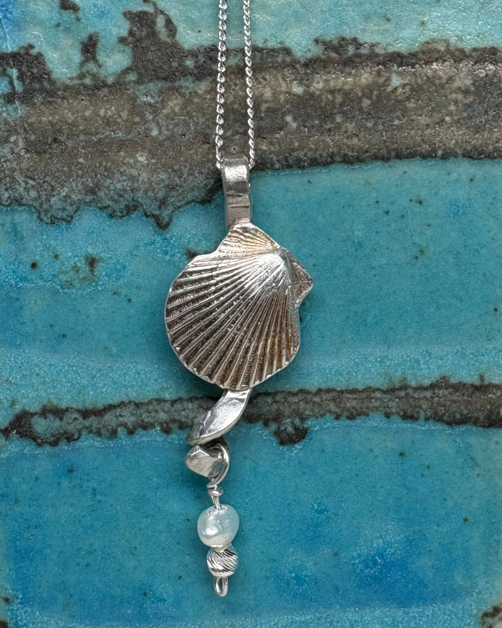 Necklace with a shell and pearl pendant on a textured blue and brown surface