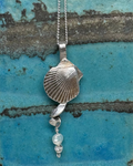 Necklace with a shell and pearl pendant on a textured blue and brown surface