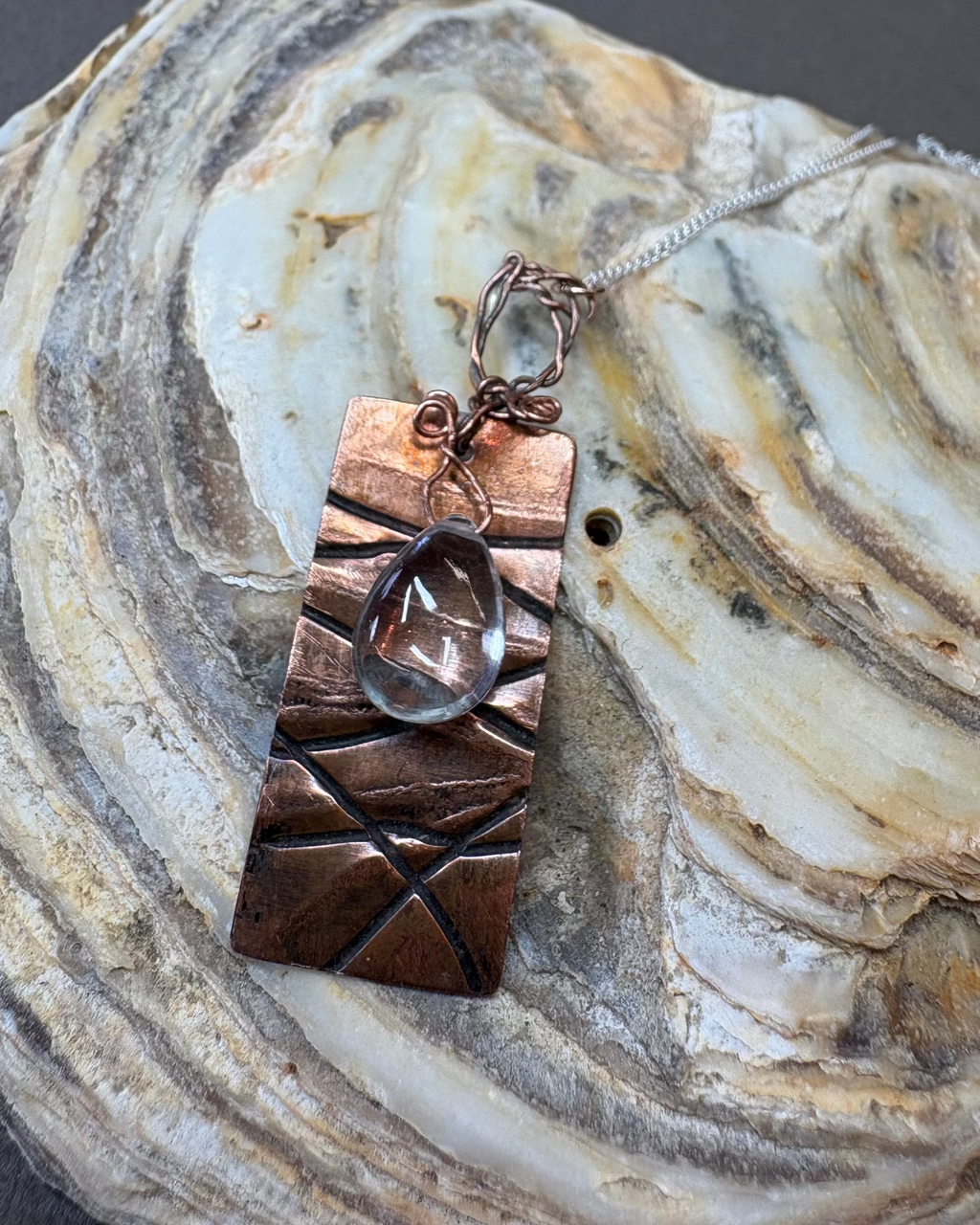Copper pendant necklace with a quartz teardrop crystal on a shell surface