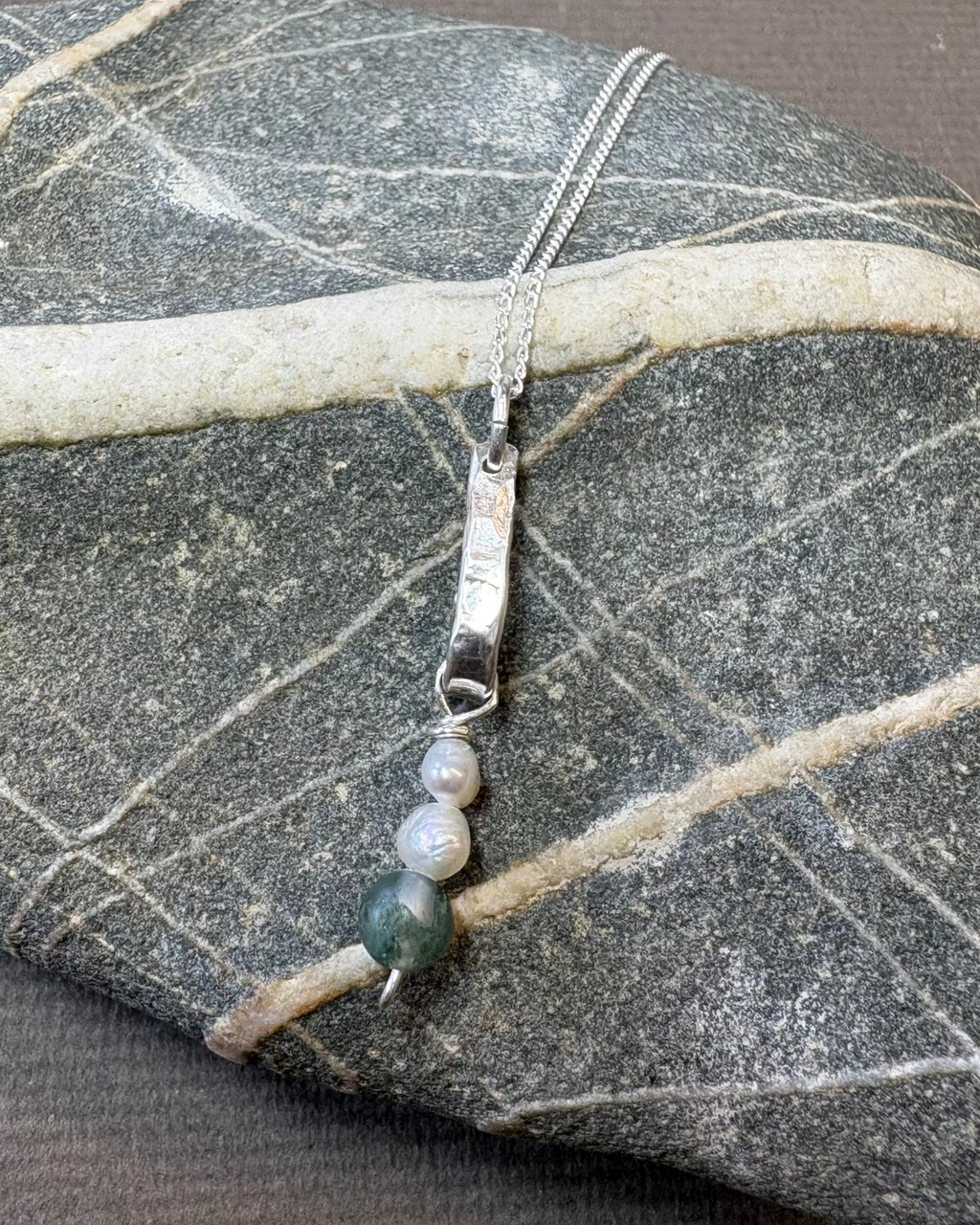 Silver bar necklace with pearls and moss agate beads on a stone surface