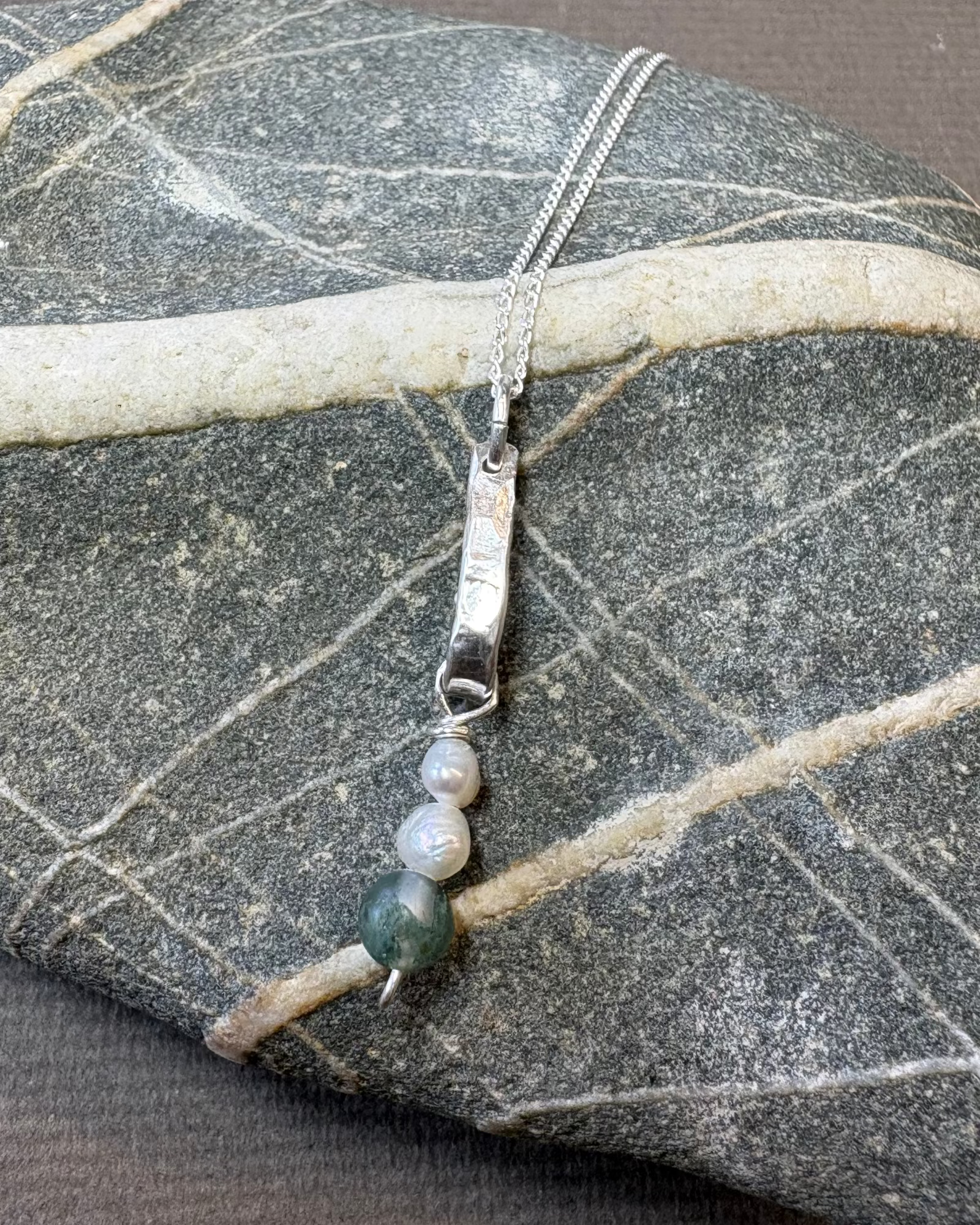 Silver bar necklace with pearls and moss agate beads on a stone surface