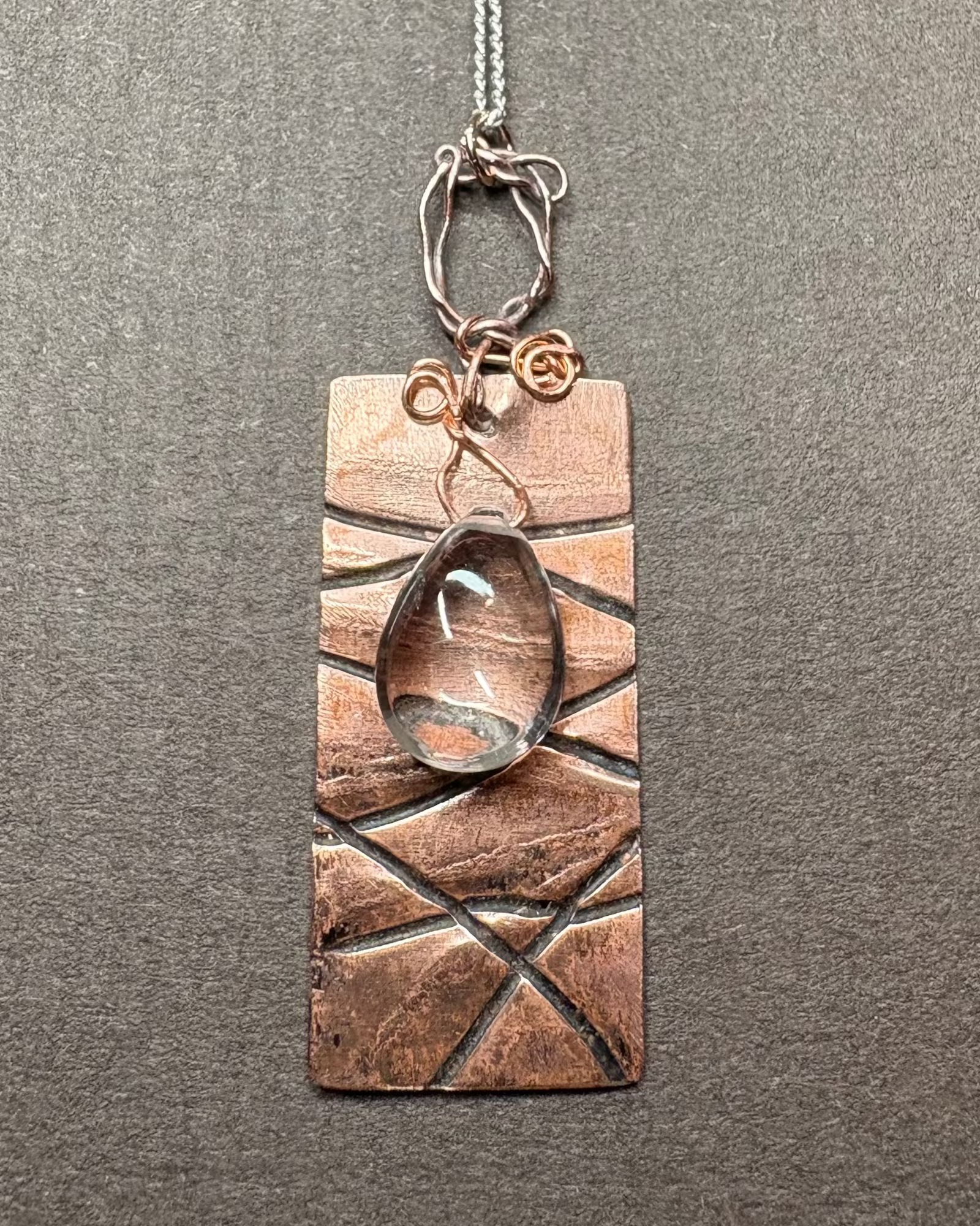 Copper pendant with deep line texture with wire work holding a clear pear shaped quartz crystal silver fine curb chain 