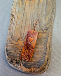Copper necklace with a heart-stamped pendant on driftwood background