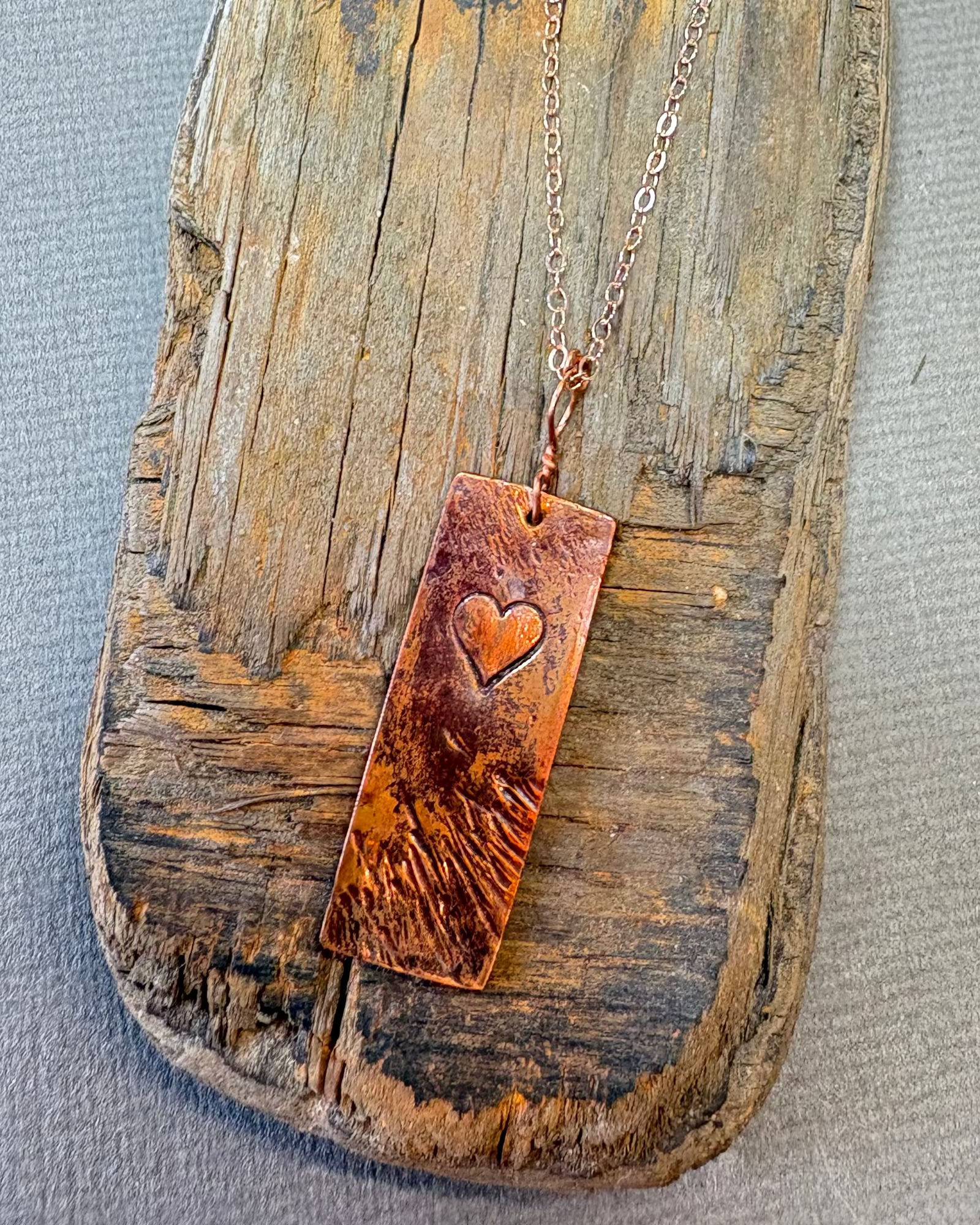 Copper necklace with a heart-stamped pendant on driftwood background