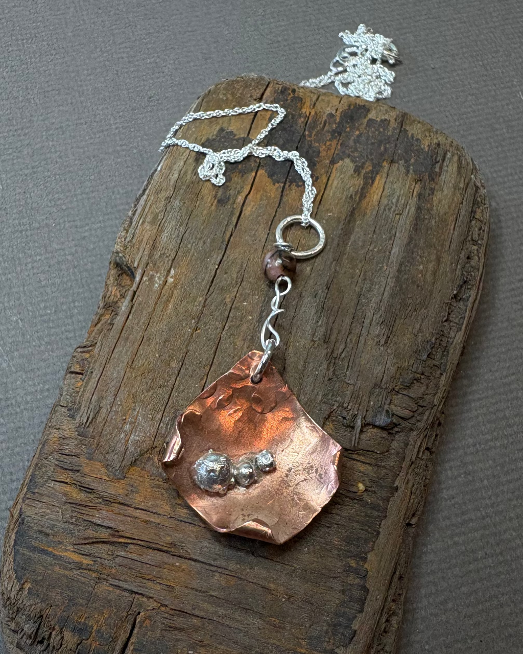 Copper and silver curled pendant on a silver chain on a driftwood 