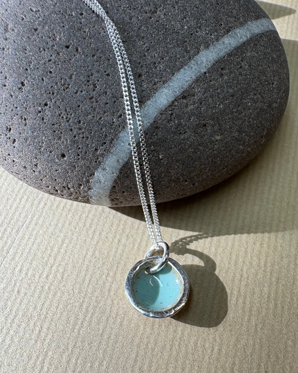Silver pool necklace  with turquoise enamel pictured by a pebble