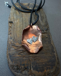 Copper pendant with silver heart designs on a wooden block