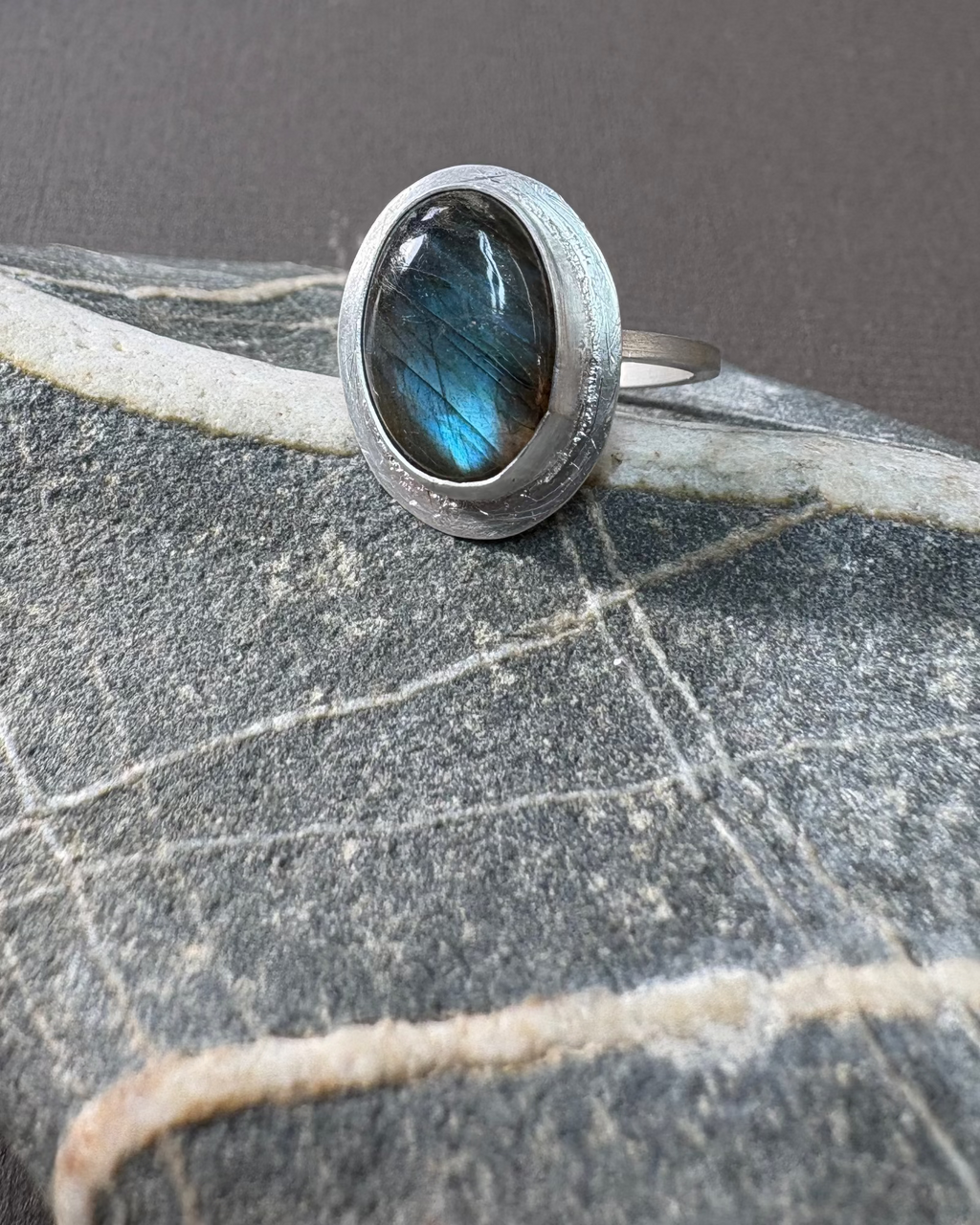 Silver ring with a bezel set labradorite gemstone on a textured surface
