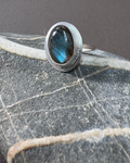 Silver ring with a bezel set labradorite gemstone on a textured surface