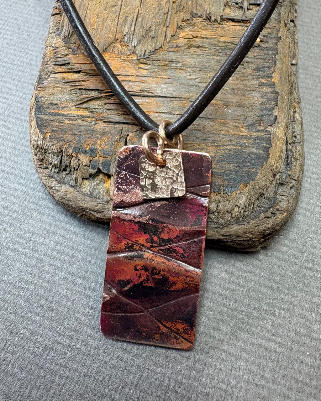 copper oxidised rectangular pendant on a wooden surface