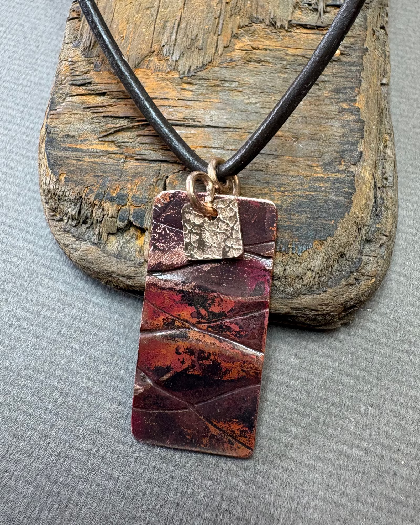 copper oxidised rectangular pendant on a wooden surface