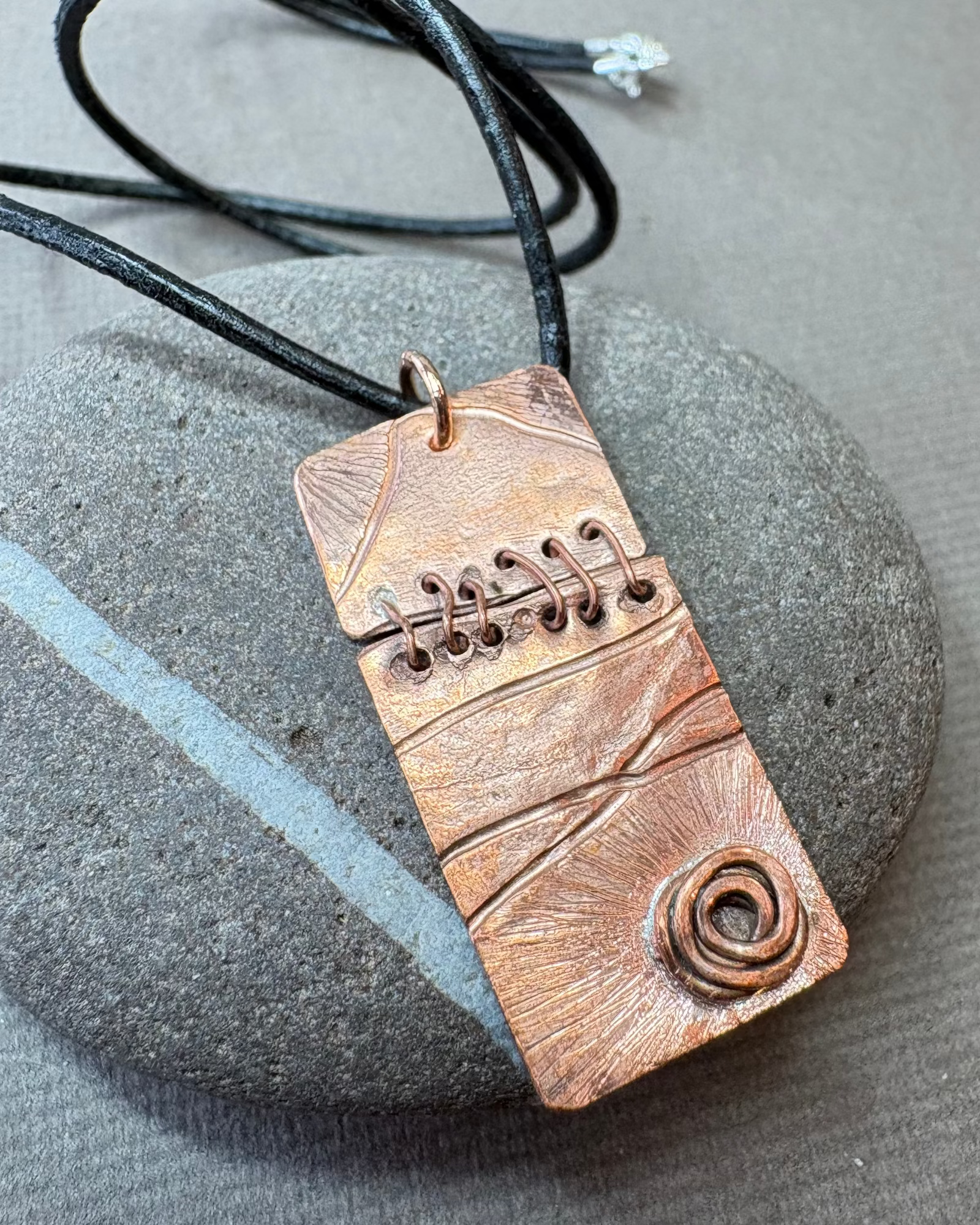 Copper sewn pendant necklace with a black leather cord on a pebble