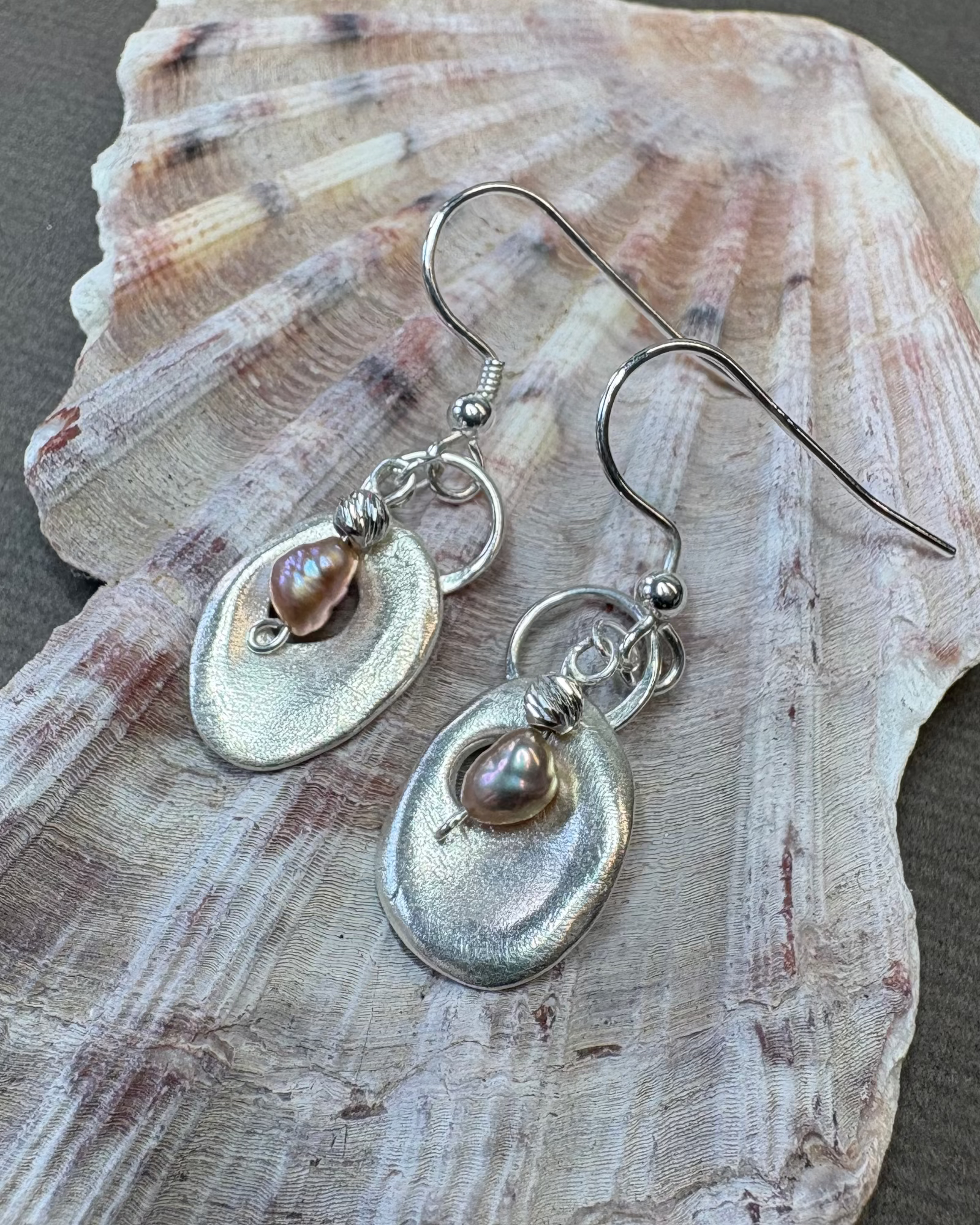Silver holey shell earrings with hanging pearl on a large shell