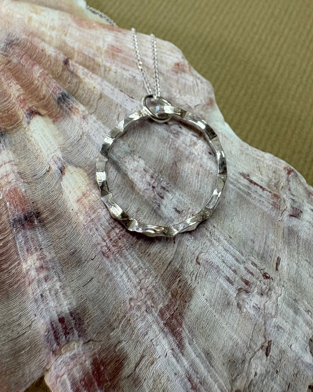 Silver necklace with a circular pendant on a shell against a gold background