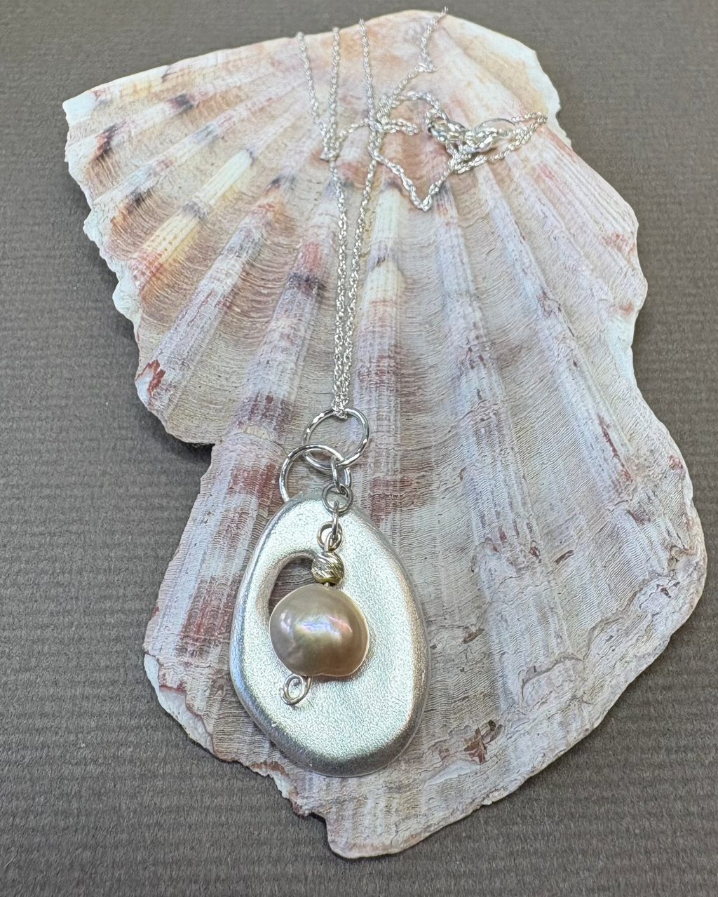 Silver necklace with a holey shell pendant with natural pearl charm on a shell