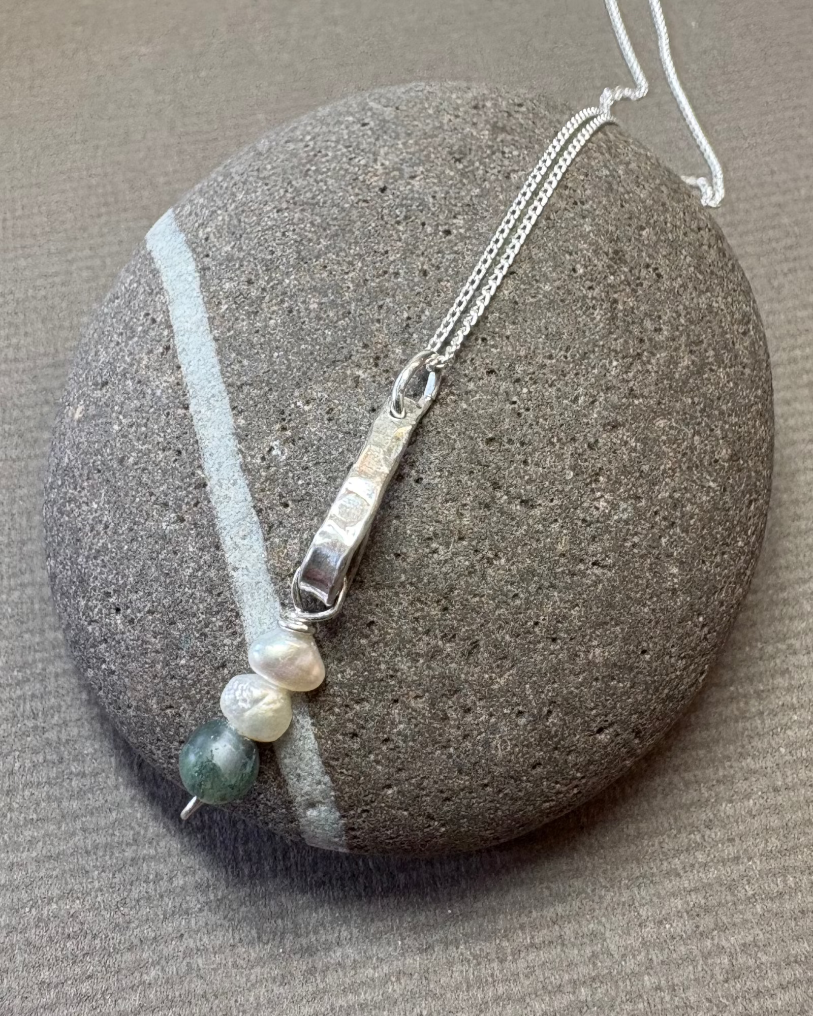 Silver bar necklace with pearls and moss agate beads on a pebble surface