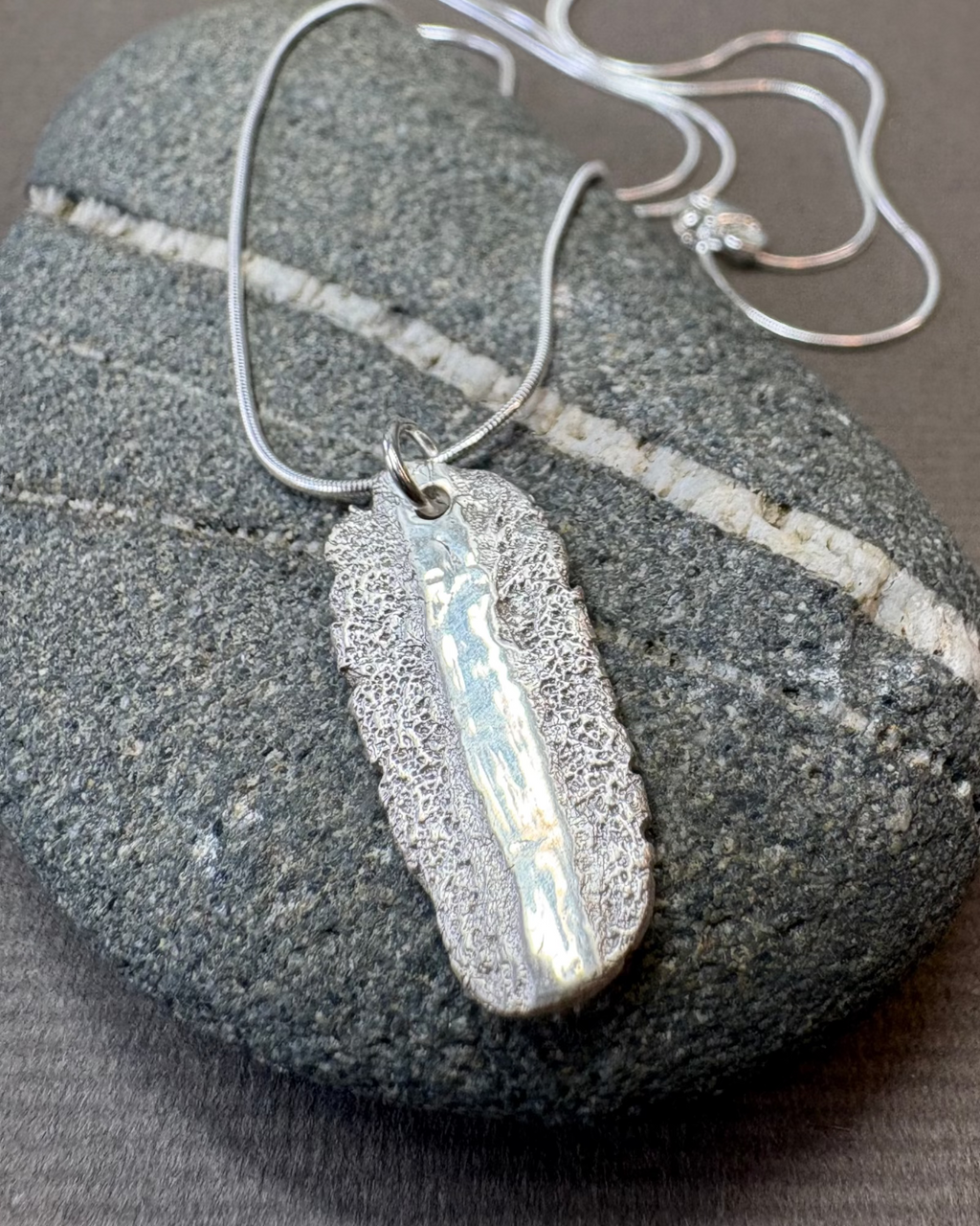 Silver pendant shiny and textured sand necklace on a stone surface