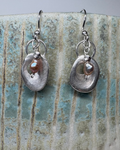Pair of silver earrings with a central pearl on a textured ceramic surface.