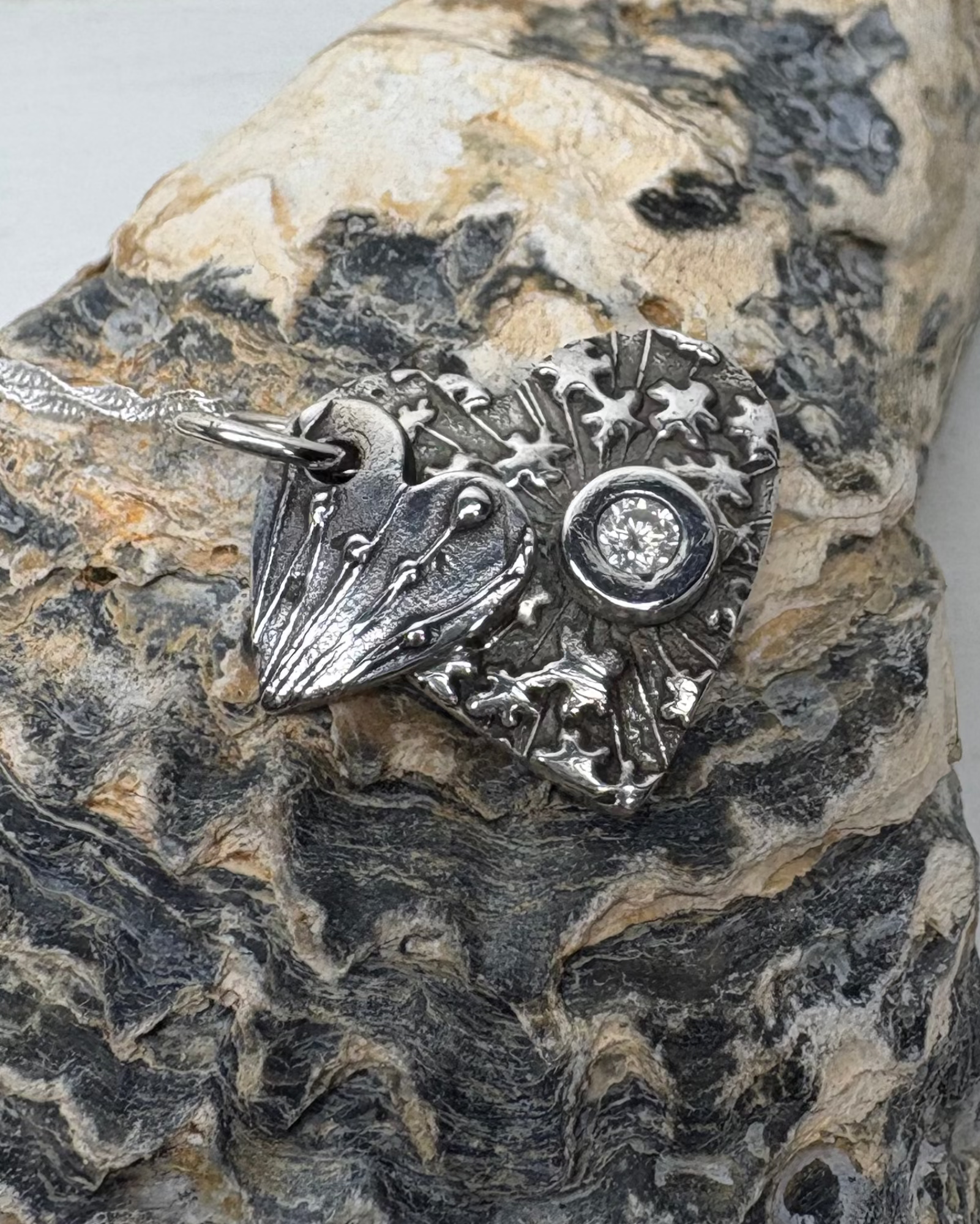 Silver oxidised double heart pendant with textured seed head designs with a white cubic zirconia set on larger heart with silver chain pictured on a textured shell