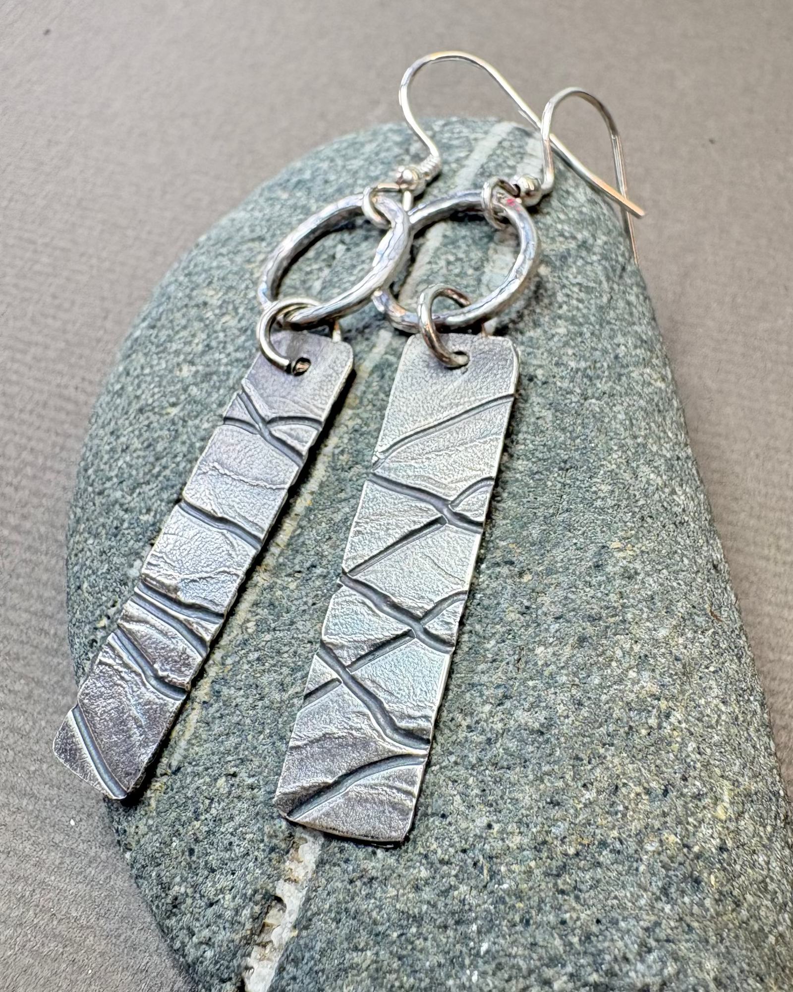 Silver hoop and texture earrings on a textured pebble surface