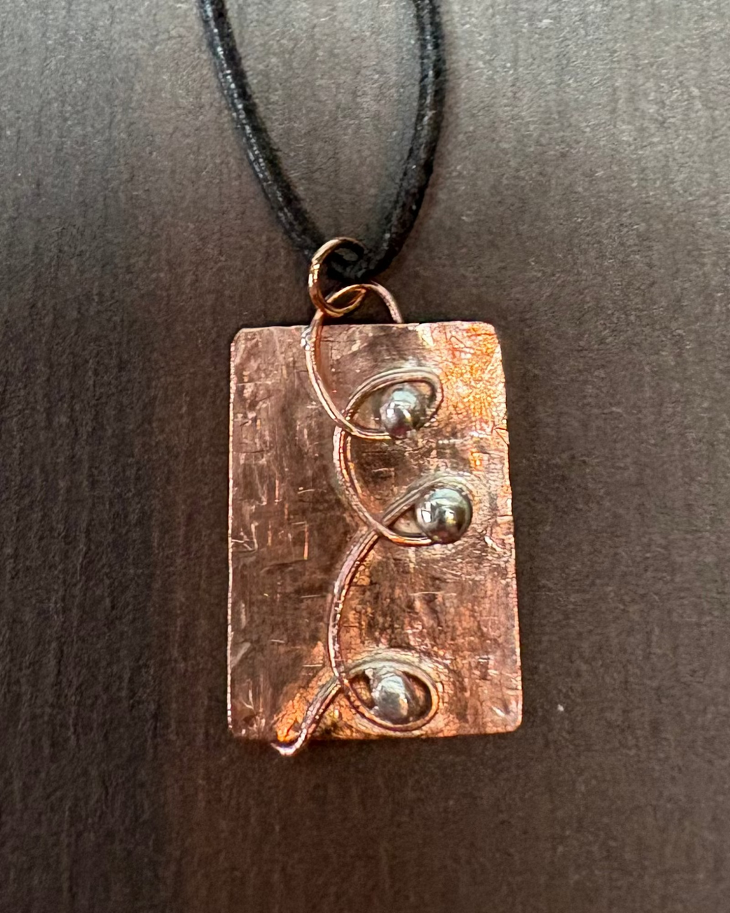Copper pendant necklace with silver balls in swirls of copper wire on a dark background