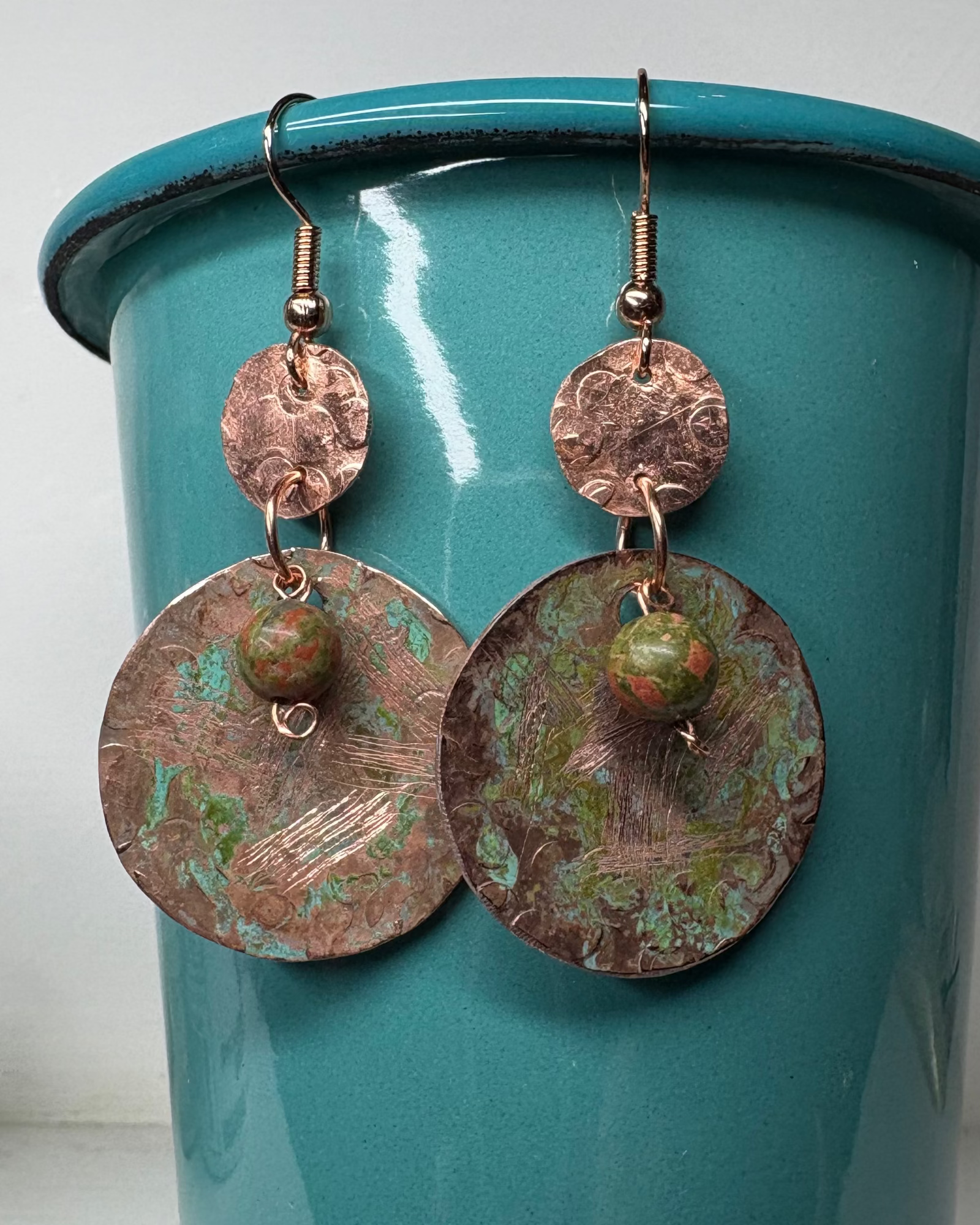 Copper circle earrings with green patina and texture with unakite stone beads on a teal background