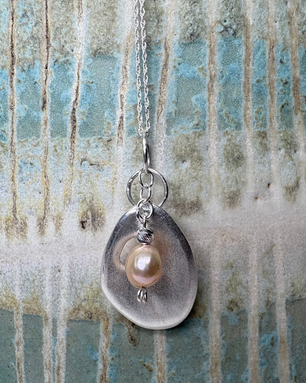 Necklace with a silver pendant featuring a pearl on a textured background