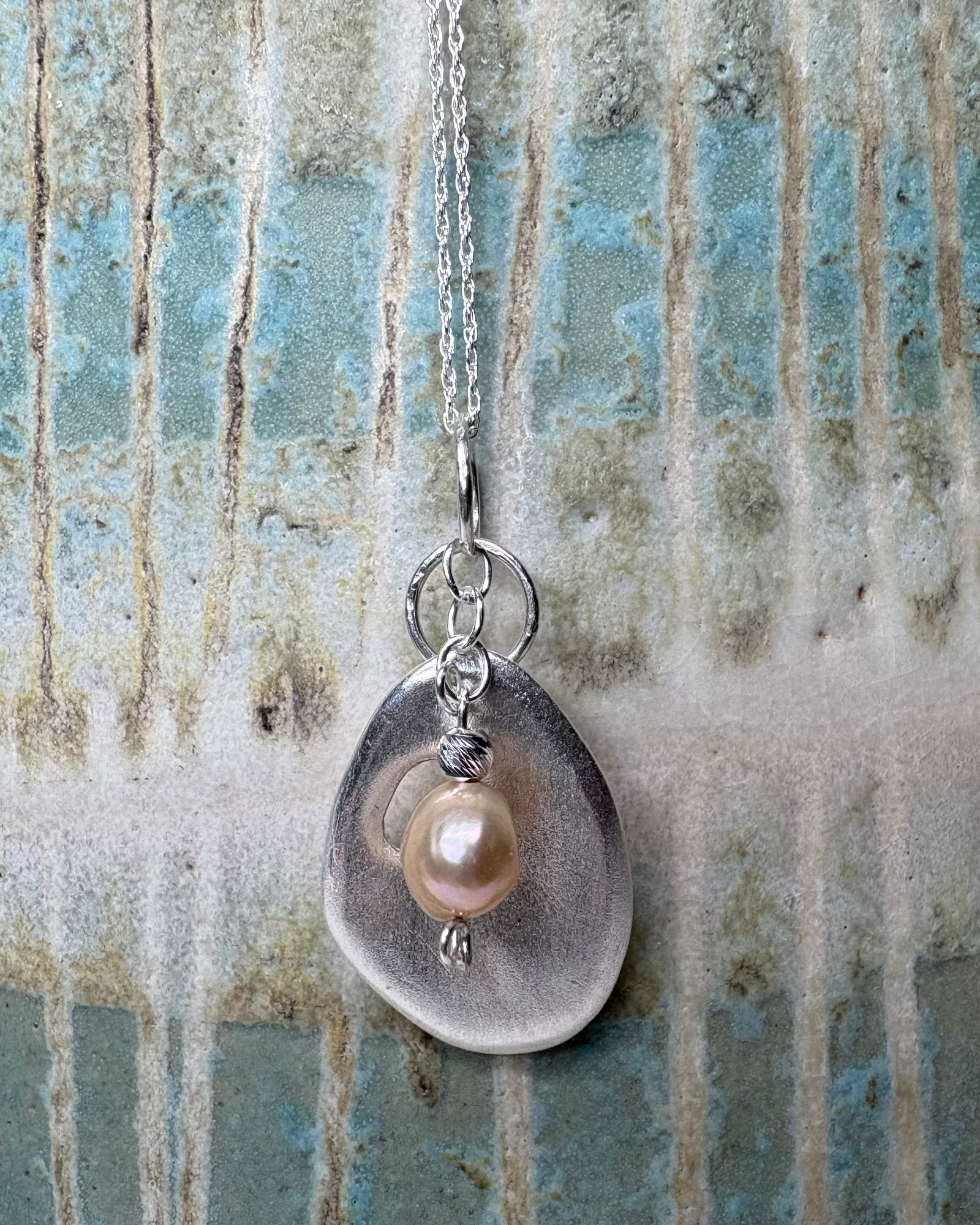 Necklace with a silver pendant featuring a pearl on a textured background