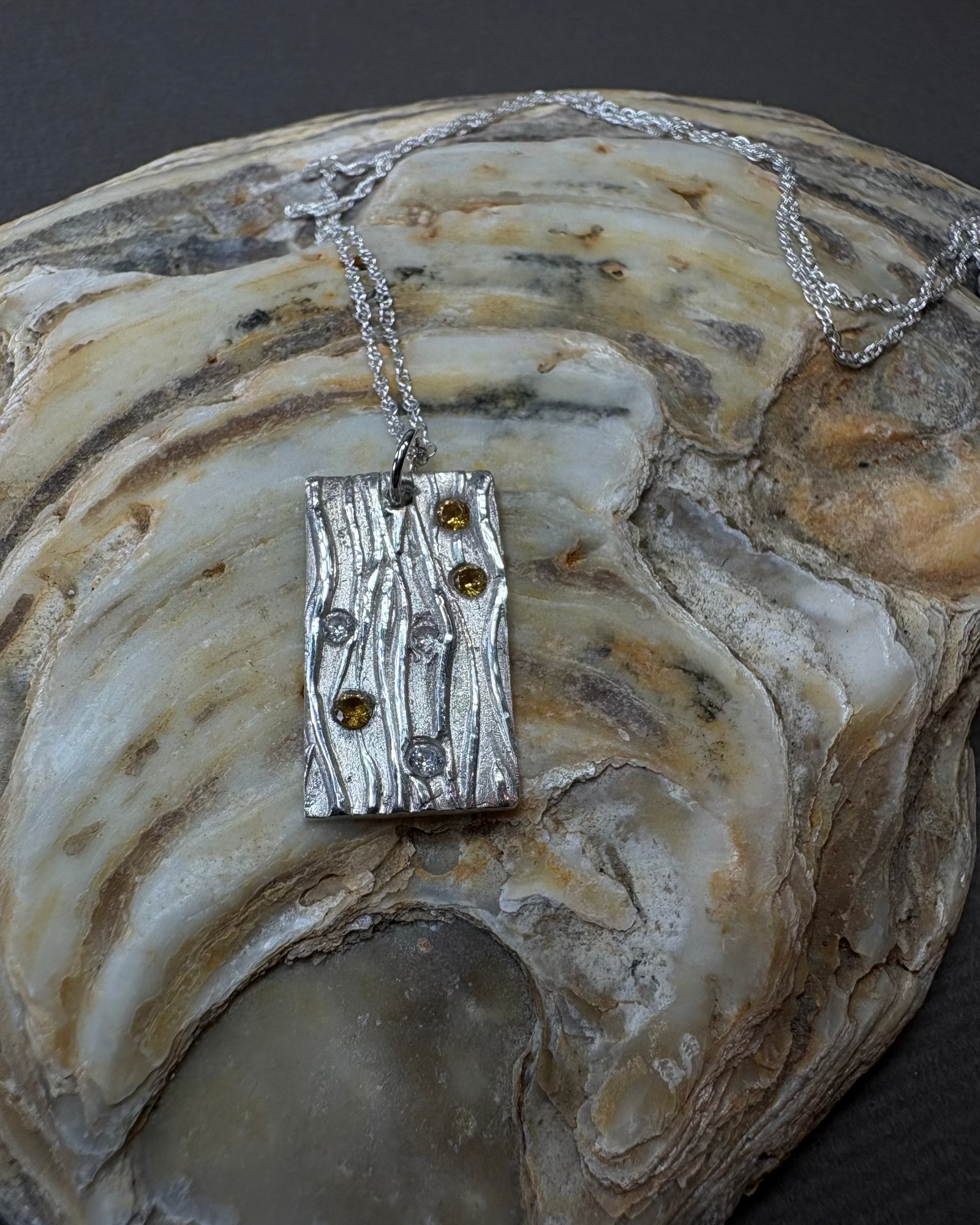 Silver stream pendant with cubic zirconia on a necklace, displayed on a shell.