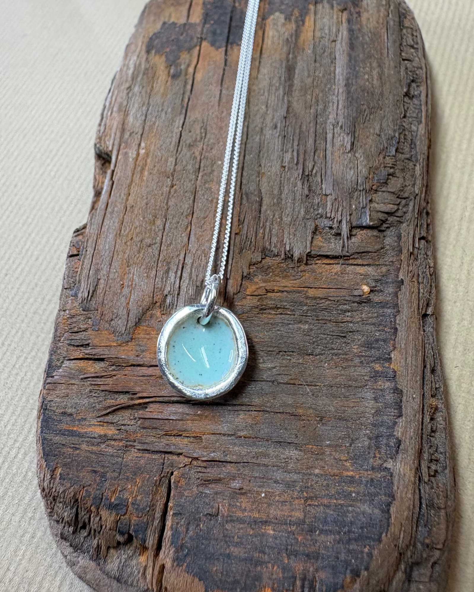 Silver pool necklace with turquoise enamel on a piece of driftwood