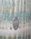 Silver cornish pebble textured necklace on a silver chain pictured against ceramic surface